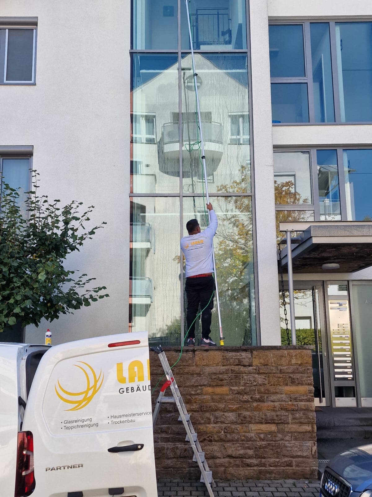 Beschrifteter Largo-Transporter mit Leiter und Ausrüstung vor dem Objekt während der Glasreinigung
